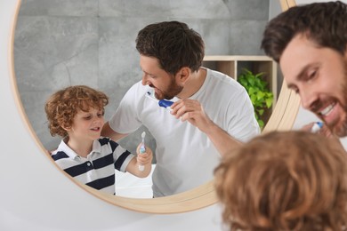 Father and his son brushing teeth together near mirror in bathroom
