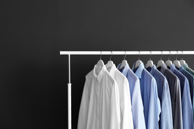 Photo of Wardrobe rack with men's clothes against grey background. Space for text