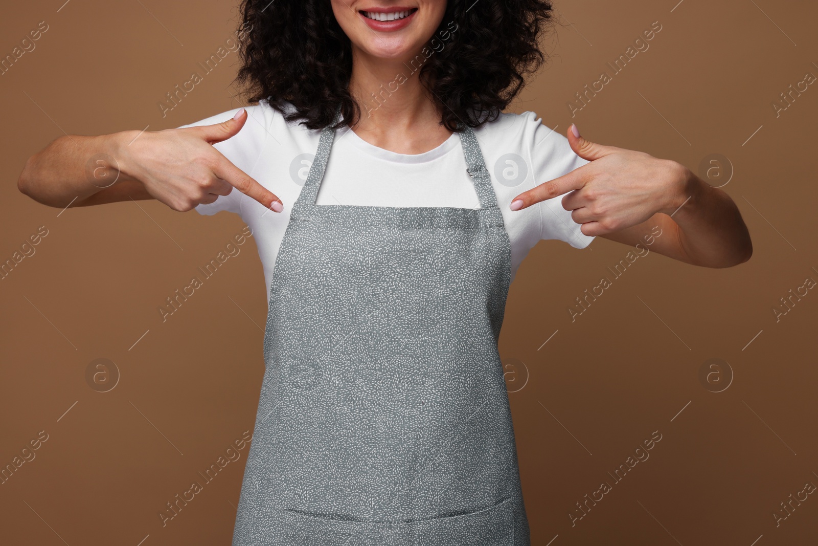 Photo of Woman pointing at kitchen apron on brown background, closeup. Mockup for design