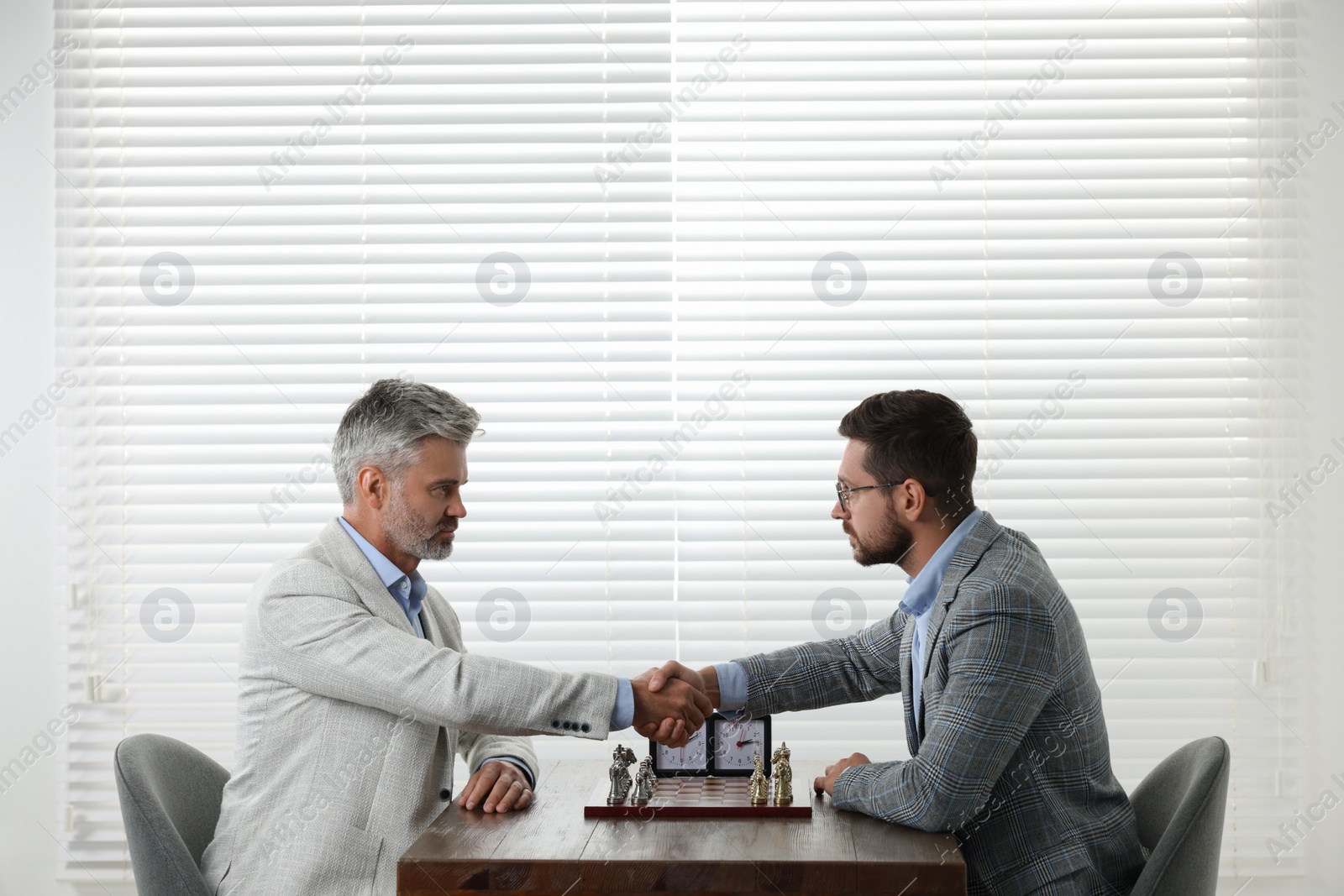 Photo of Men shaking their hands during chess tournament at table indoors