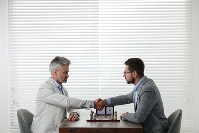 Photo of Men shaking their hands during chess tournament at table indoors