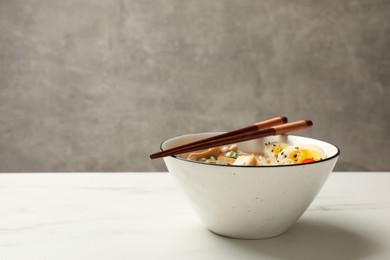 Bowl of delicious ramen and chopsticks on white marble table, space for text. Noodle soup