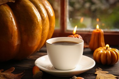 Photo of Cup of hot drink and pumpkin shaped candles on wooden table near window, closeup. Cozy autumn atmosphere