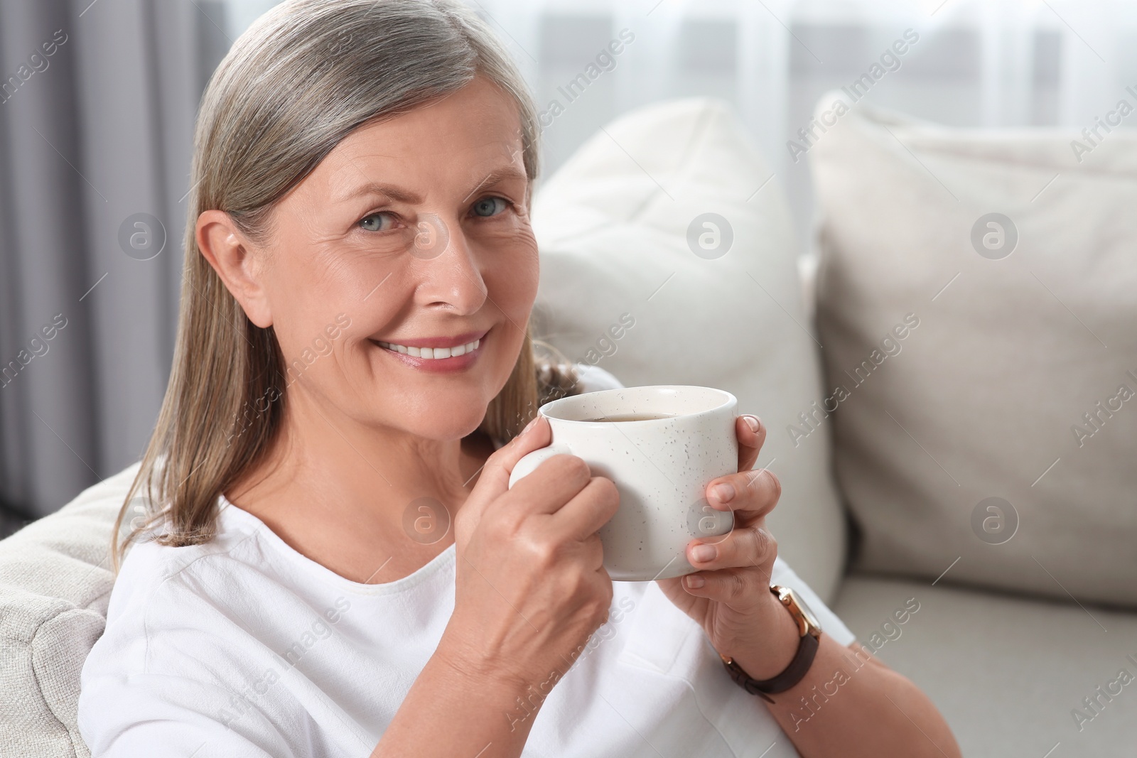 Photo of Senior woman with cup of tea on sofa at home