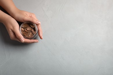 Photo of Woman holding glass jar with coins on light grey background, closeup. Space for text