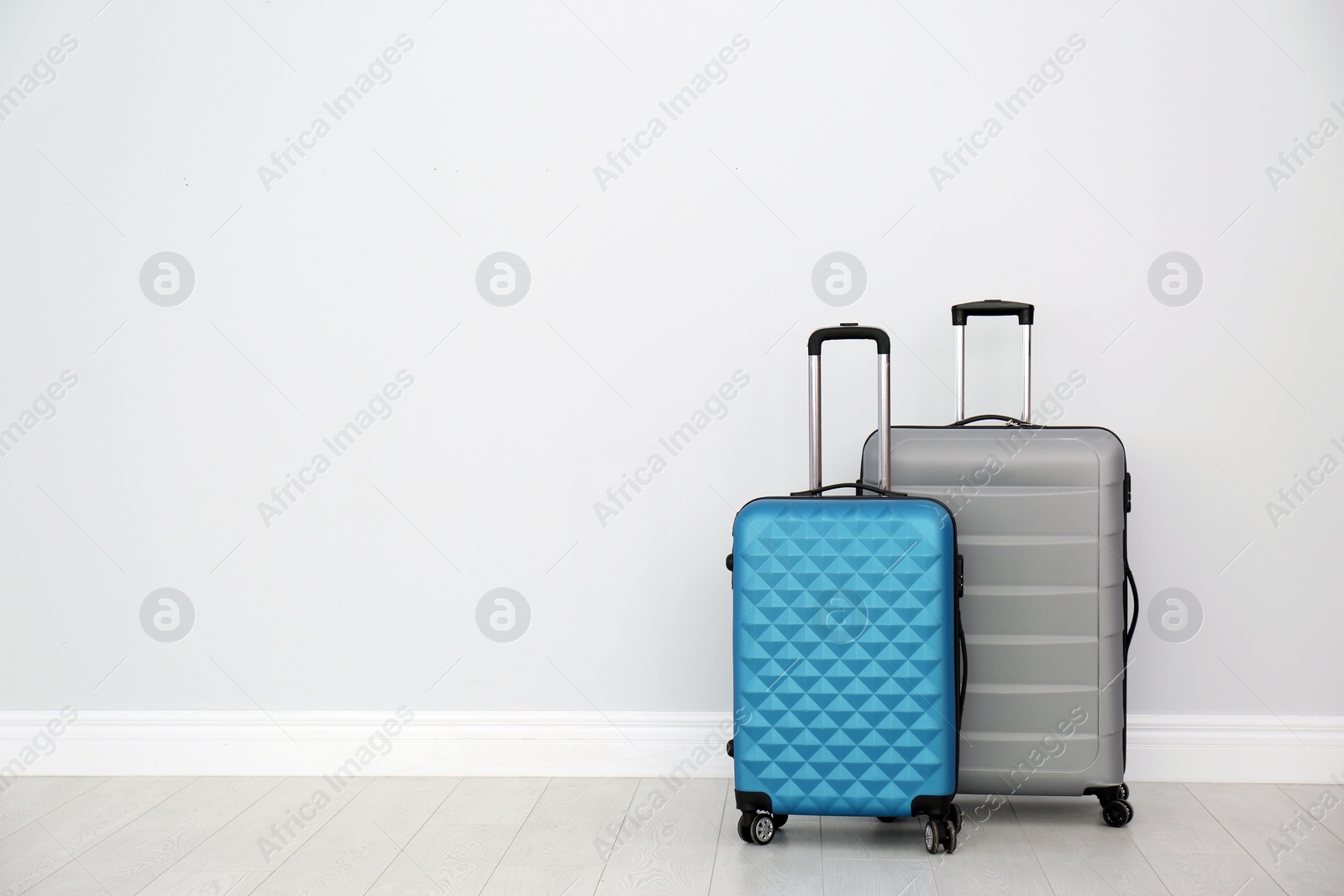 Photo of Modern suitcases on floor near light wall. Space for text