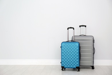 Photo of Modern suitcases on floor near light wall. Space for text