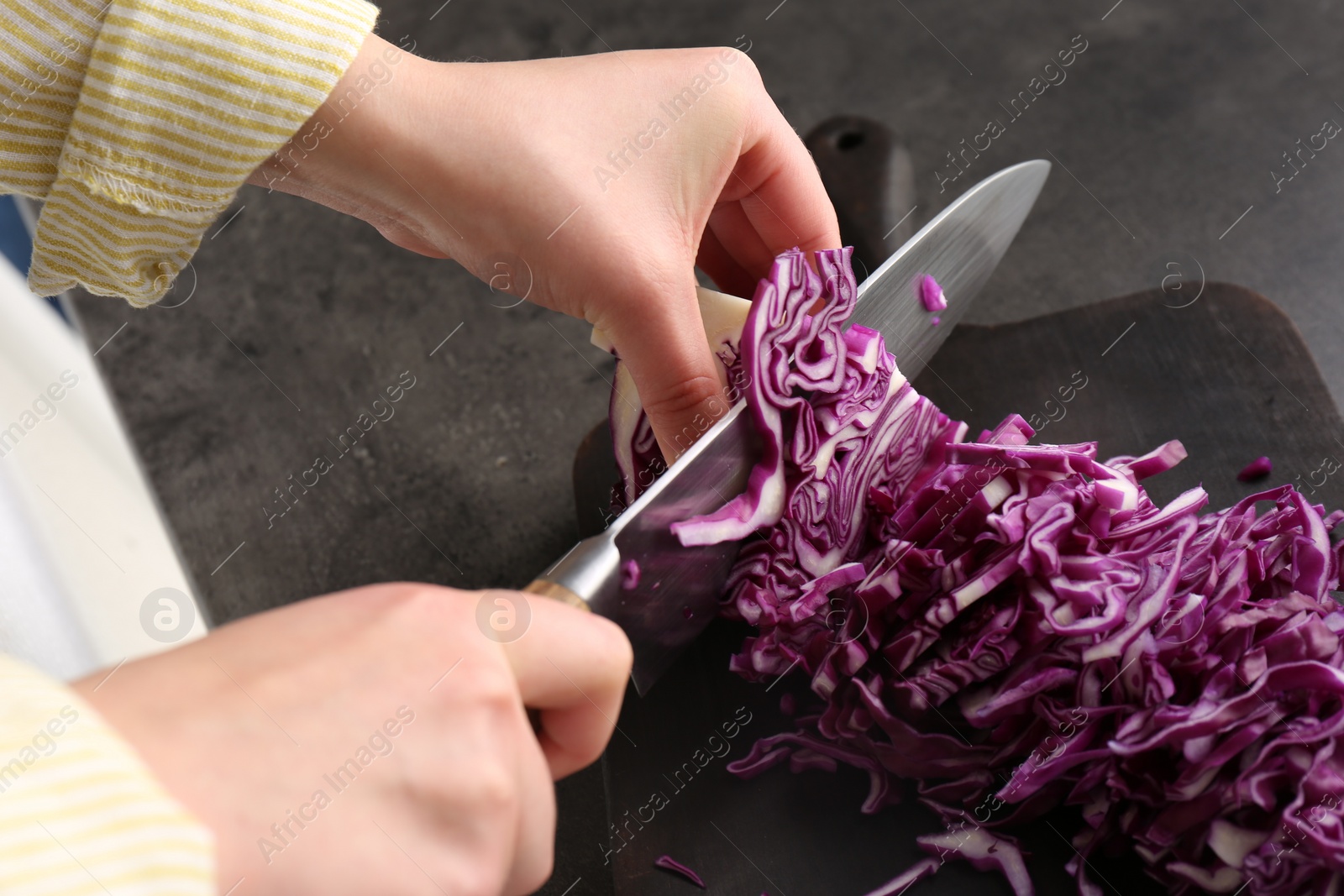 Photo of Woman cutting fresh red cabbage at black table, closeup