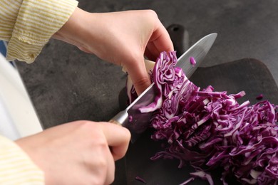 Woman cutting fresh red cabbage at black table, closeup