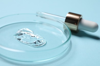 Petri dish with sample of cosmetic serum and pipette on light blue background, closeup