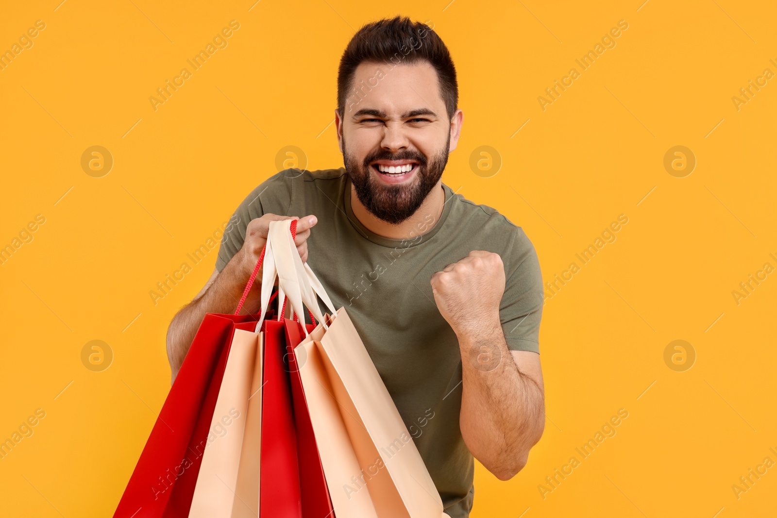 Photo of Excited man with many paper shopping bags on orange background