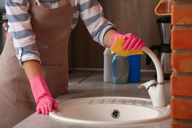 Photo of Woman cleaning tap with rag in kitchen, closeup