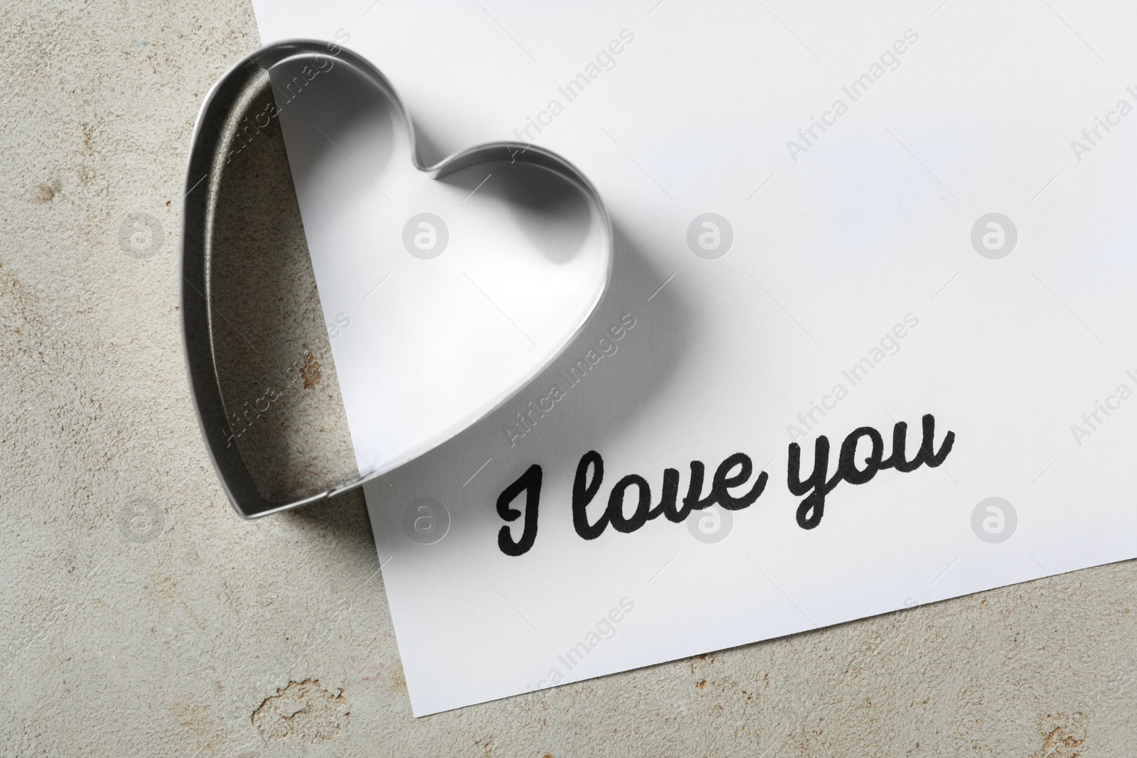 Photo of Card with phrase I Love You and heart shaped cookie cutter on grey table, flat lay