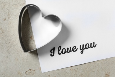 Card with phrase I Love You and heart shaped cookie cutter on grey table, flat lay