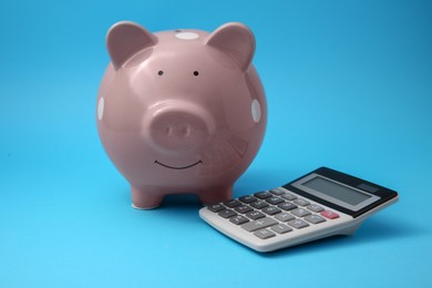 Photo of Piggy bank and calculator on light blue background