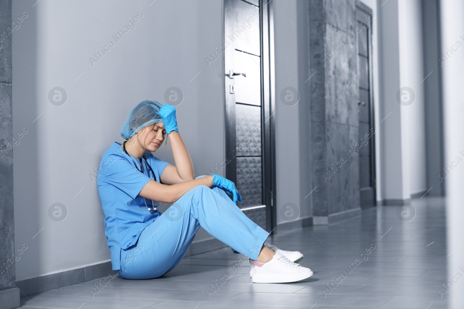 Photo of Exhausted doctor sitting on floor in hospital, space for text