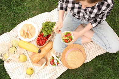 Girl having picnic on green grass in park, above view