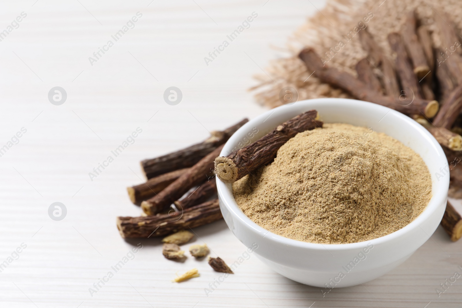 Photo of Powder in bowl and dried sticks of liquorice root on white table, space for text