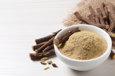 Powder in bowl and dried sticks of liquorice root on white table, space for text