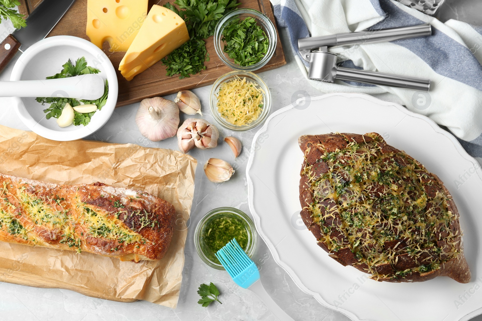 Photo of Loaves of tasty homemade garlic bread with cheese and herbs on grey table, flat lay