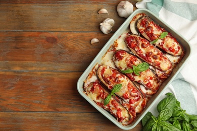 Photo of Baked eggplant with tomatoes, cheese and basil in dishware on wooden table, flat lay. Space for text