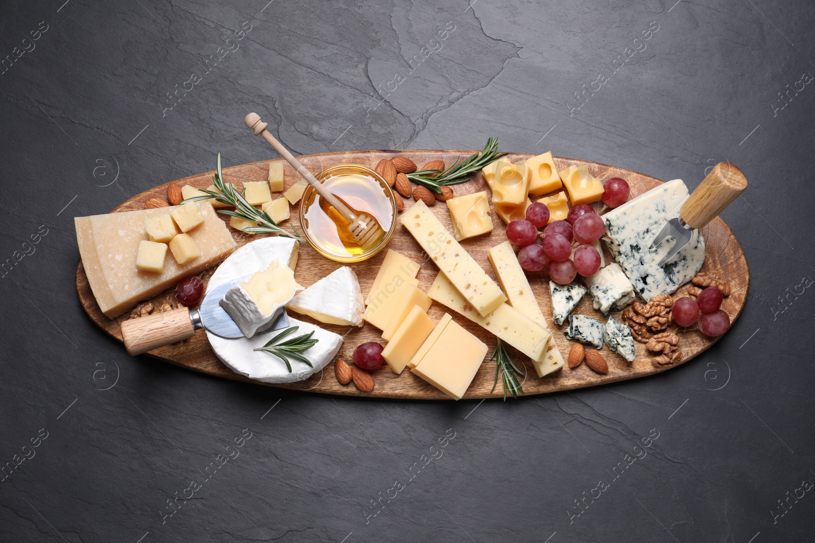 Photo of Cheese plate with honey, grapes and nuts on black table, top view