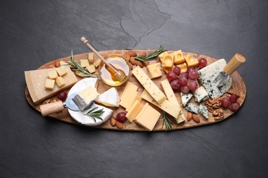 Cheese plate with honey, grapes and nuts on black table, top view