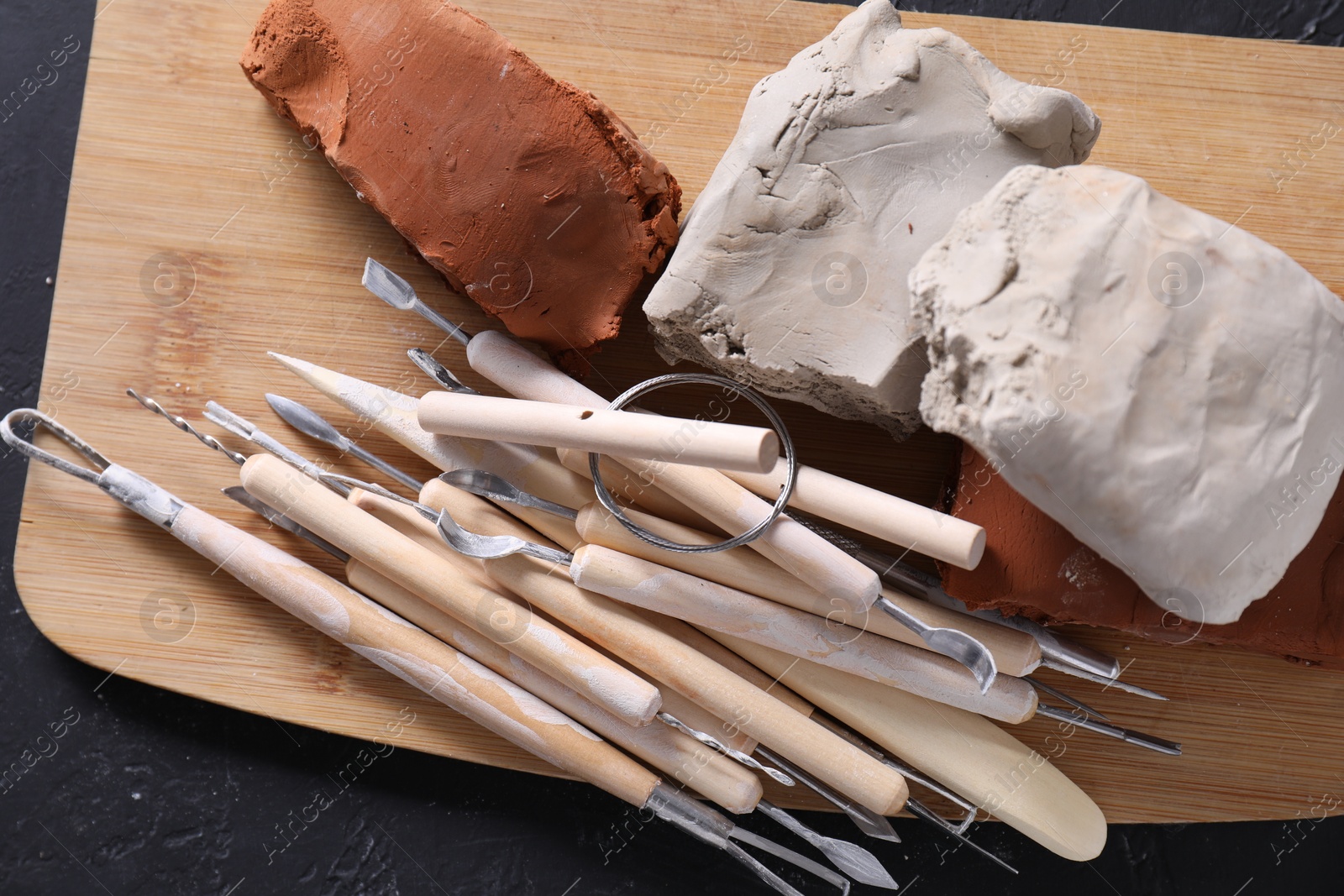 Photo of Clay and set of modeling tools on black table, top view