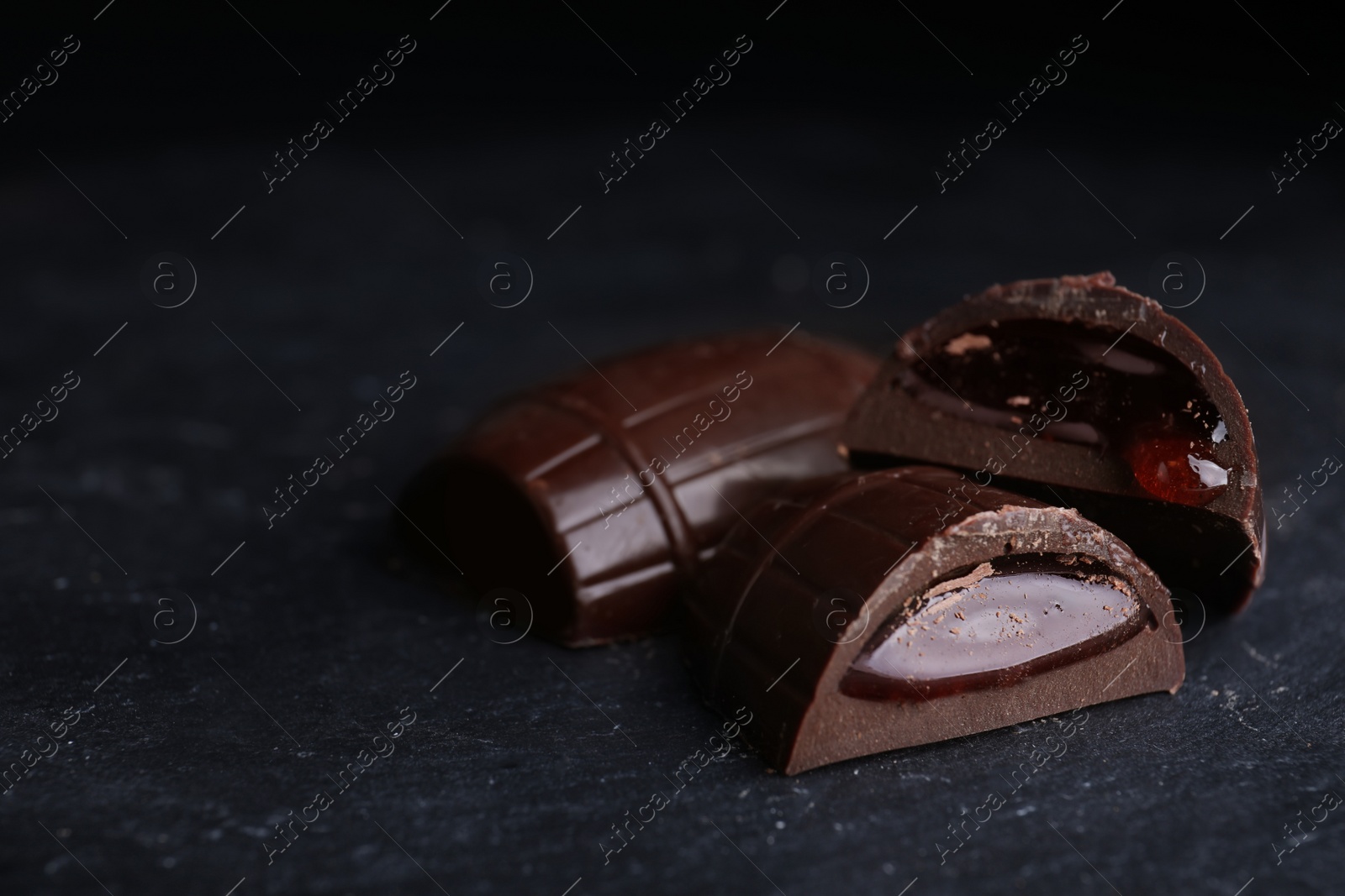 Photo of Tasty dark chocolate candies with jelly filling on black table, closeup