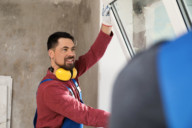 Workers in uniform installing plastic window indoors