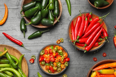Photo of Different ripe hot chili peppers on grey table, flat lay