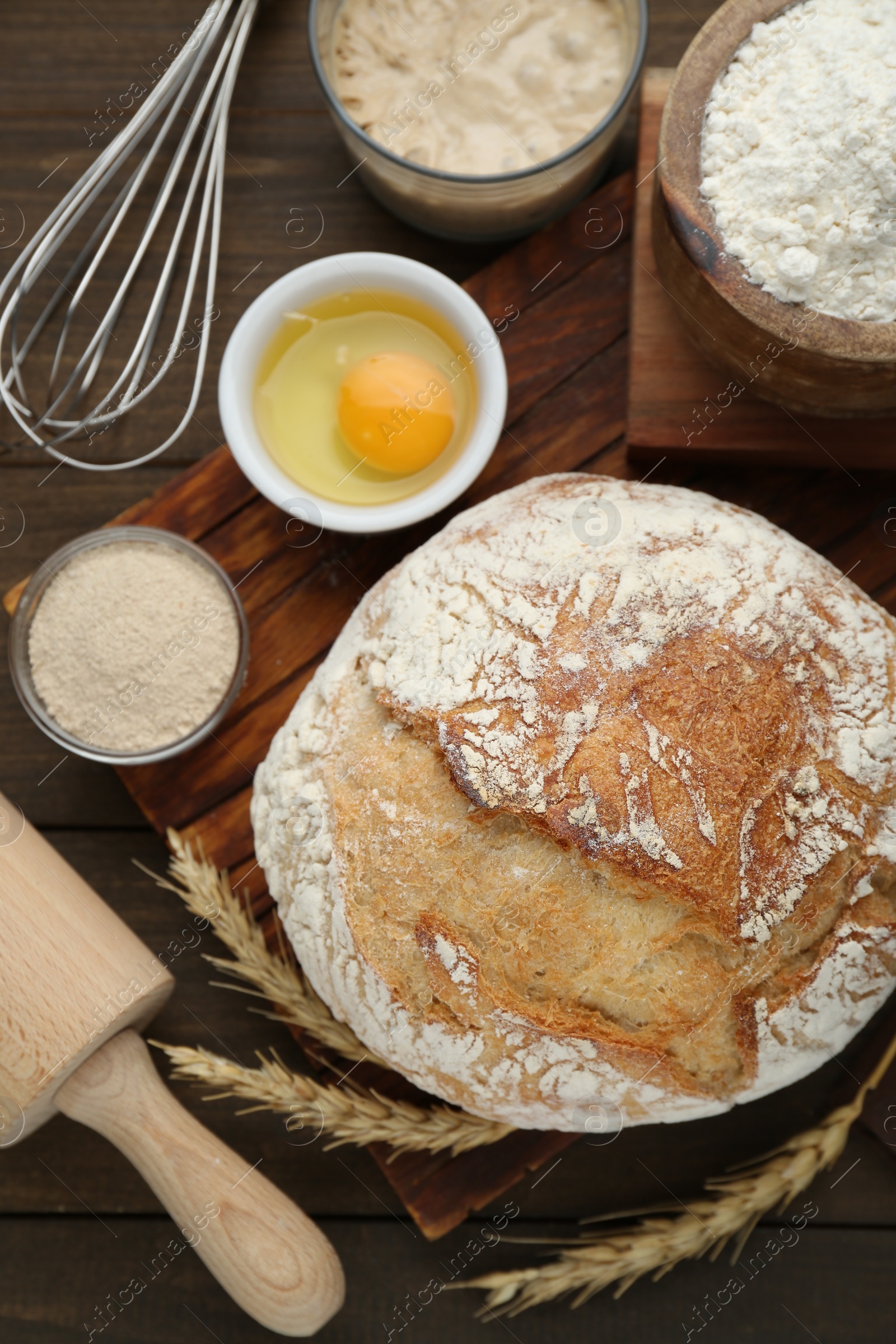 Photo of Freshly baked sourdough bread and ingredients on wooden table, flat lay