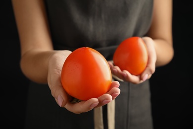 Photo of Woman holding delicious fresh persimmons on black background, closeup