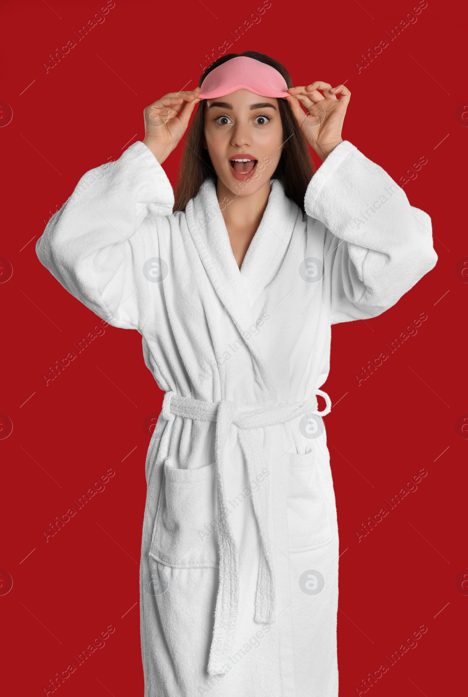 Photo of Young woman in bathrobe and eye sleeping mask on red background
