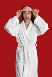 Photo of Young woman in bathrobe and eye sleeping mask on red background