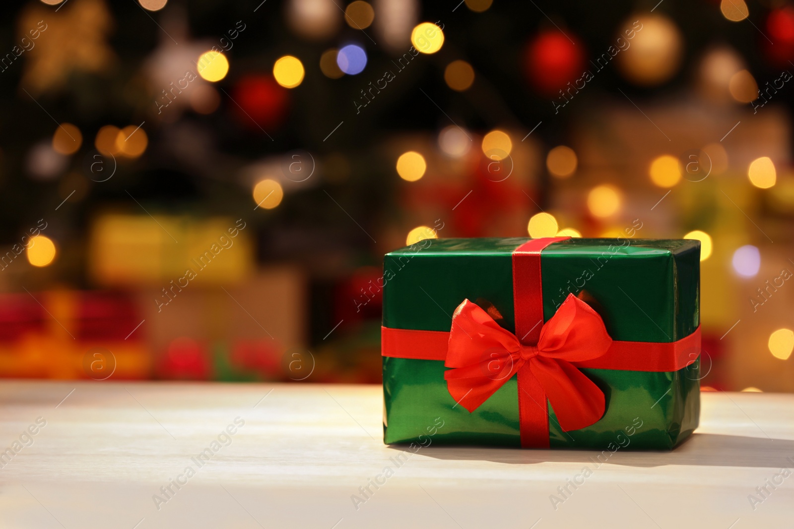 Photo of Beautifully wrapped gift box against blurred festive lights, space for text. Christmas celebration