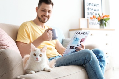 Young man with cute cat on sofa at home