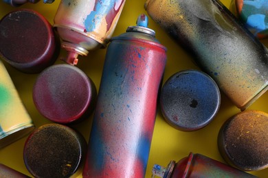 Many spray paint cans with caps on yellow background, flat lay