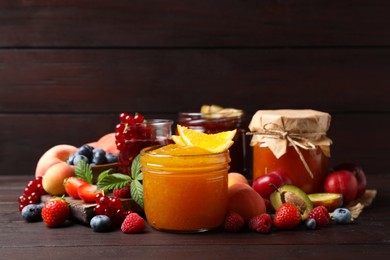 Photo of Jars with different jams and fresh fruits on wooden table