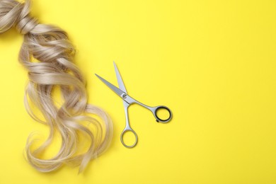 Photo of Professional hairdresser scissors, hair strands and space for text on yellow background, flat lay. Haircut tool