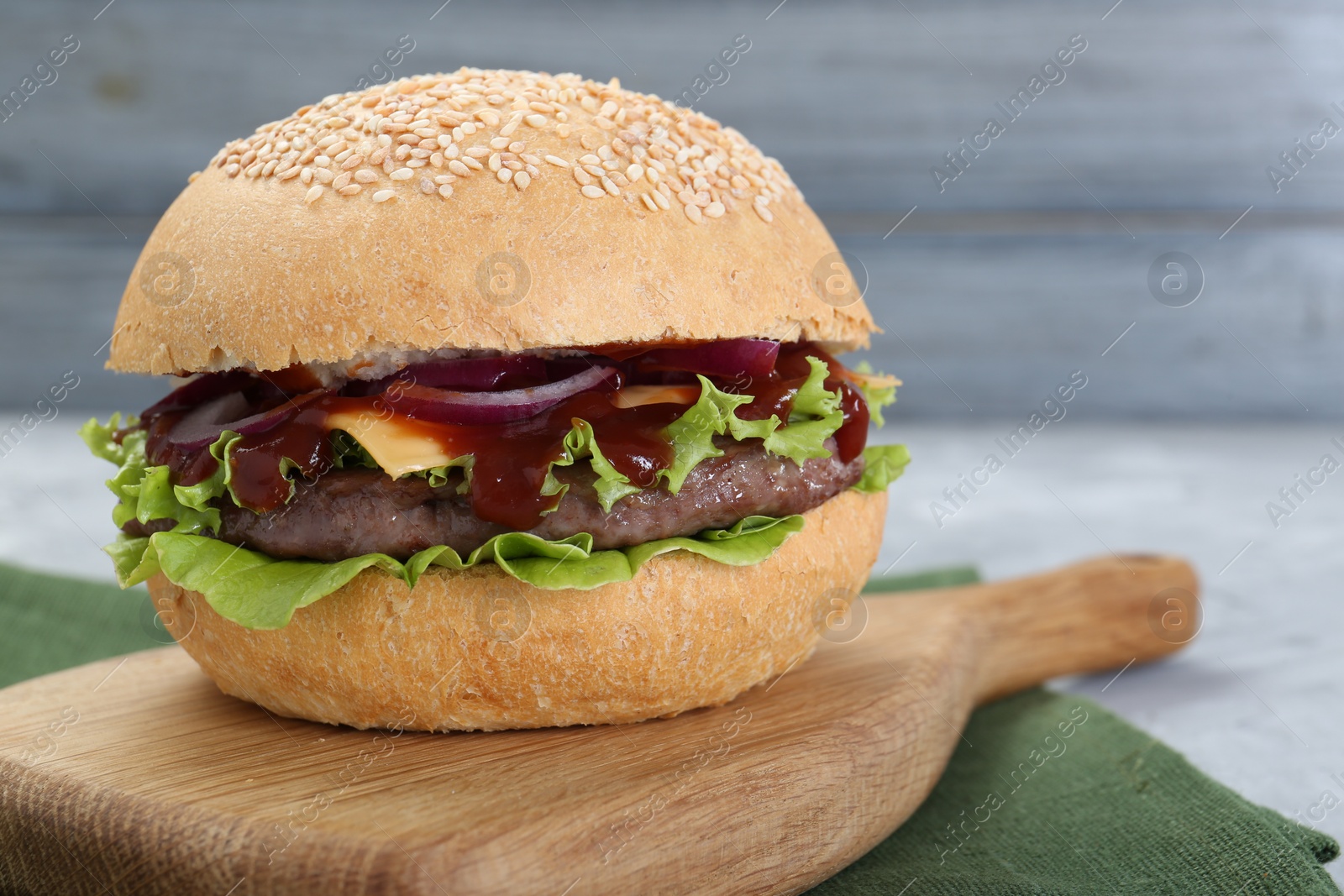 Photo of Delicious cheeseburger with lettuce, onion, ketchup and patty on table, closeup