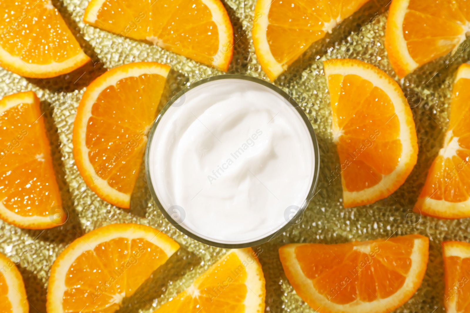 Photo of Jar of face cream surrounded by orange slices on golden textured surface, flat lay