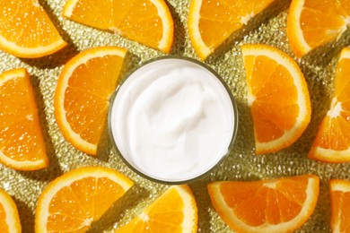 Jar of face cream surrounded by orange slices on golden textured surface, flat lay