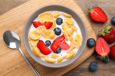 Bowl of tasty crispy corn flakes with milk and berries on wooden table, flat lay