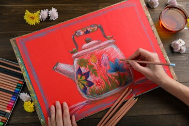 Woman drawing beautiful kettle with pastel pencil at wooden table, top view