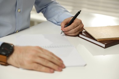 Left-handed man writing in notebook at white table, closeup