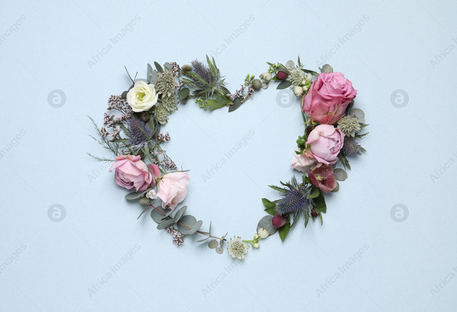 Photo of Beautiful heart made of different flowers on light blue background, flat lay. Space for text