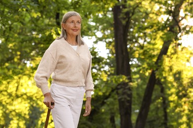 Photo of Senior woman with walking cane in park. Space for text