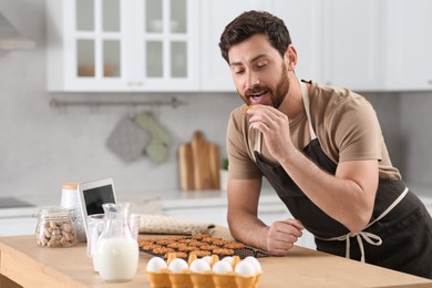 Man with freshly baked cookies watching online cooking course via tablet in kitchen