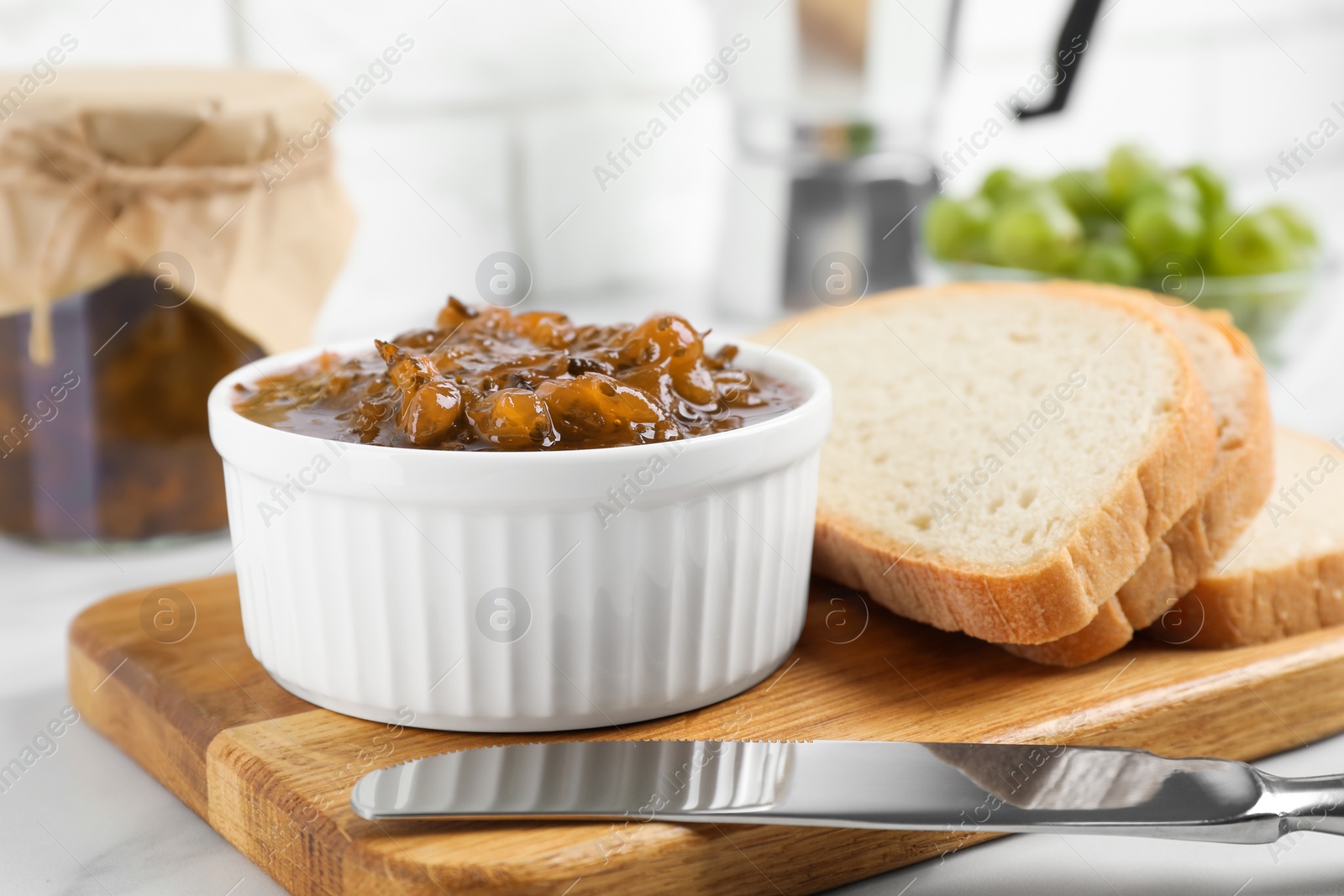 Photo of Delicious gooseberry jam and slices of bread on white table